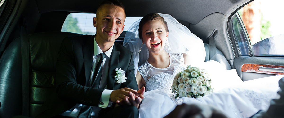 A newly married couple sitting in the back of their car.